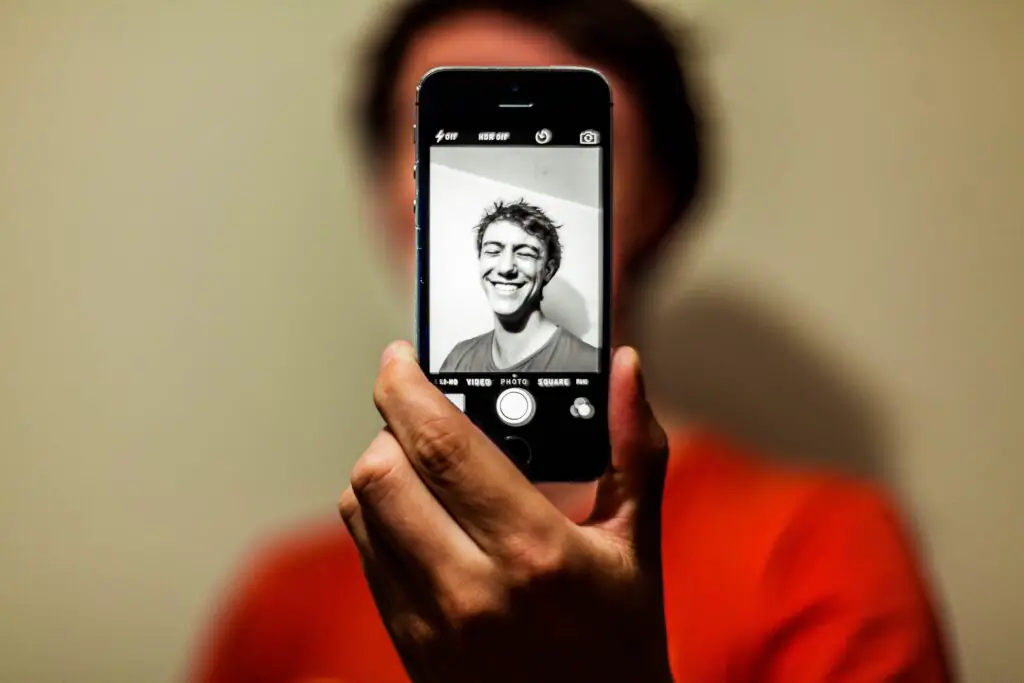 man doing a black-white photograph of himself with his phone while laughing