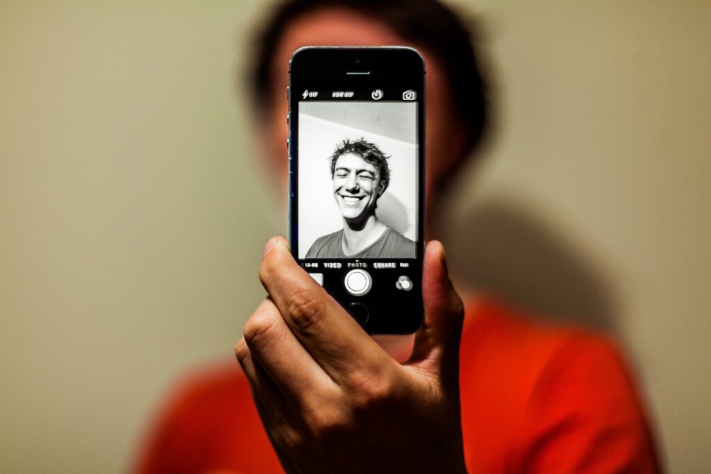 man doing a black-white photograph of himself with his phone while laughing