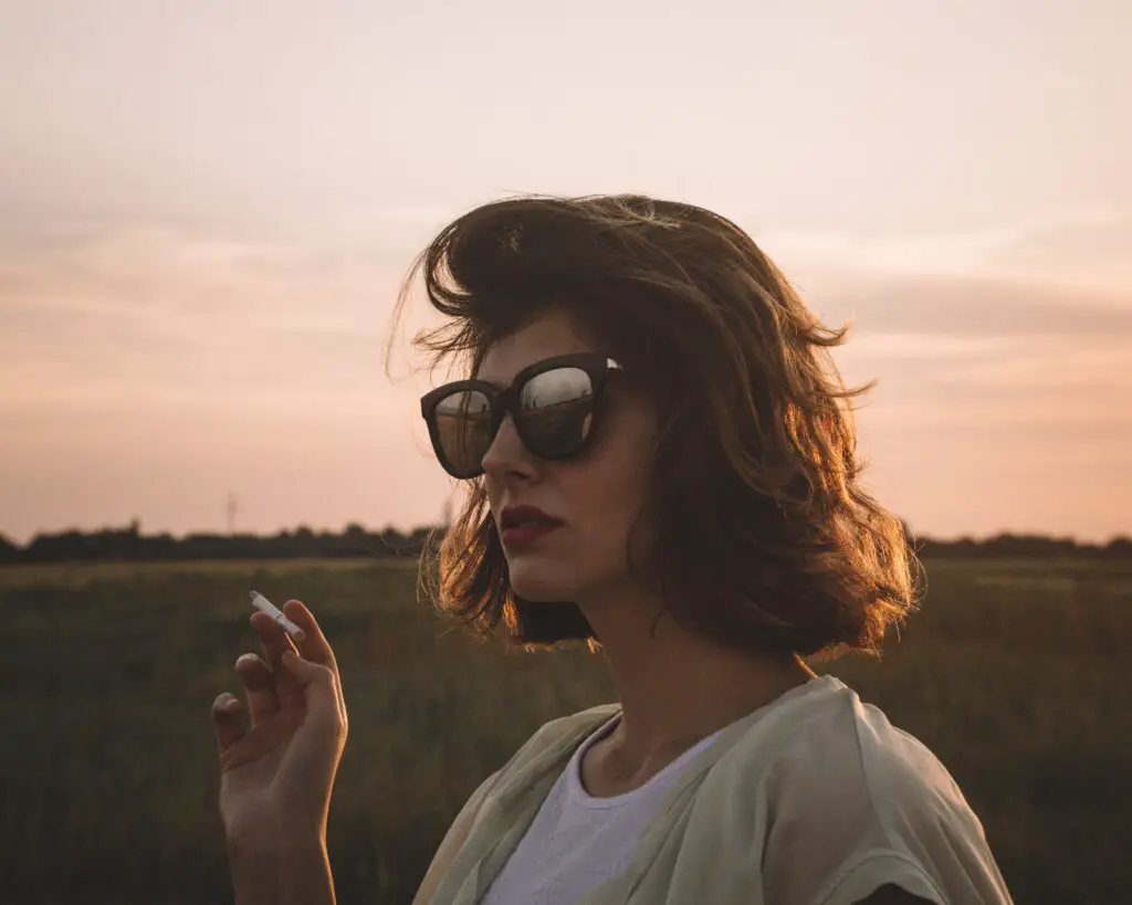 woman with sunglasses holding a cigarette during the golden hour