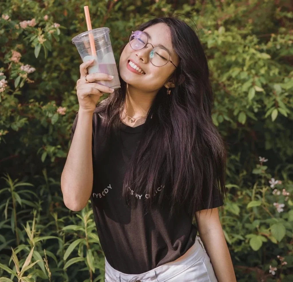 girl holding a delicious beverage drink outside while smiling and wearing glasses outside in her garden 