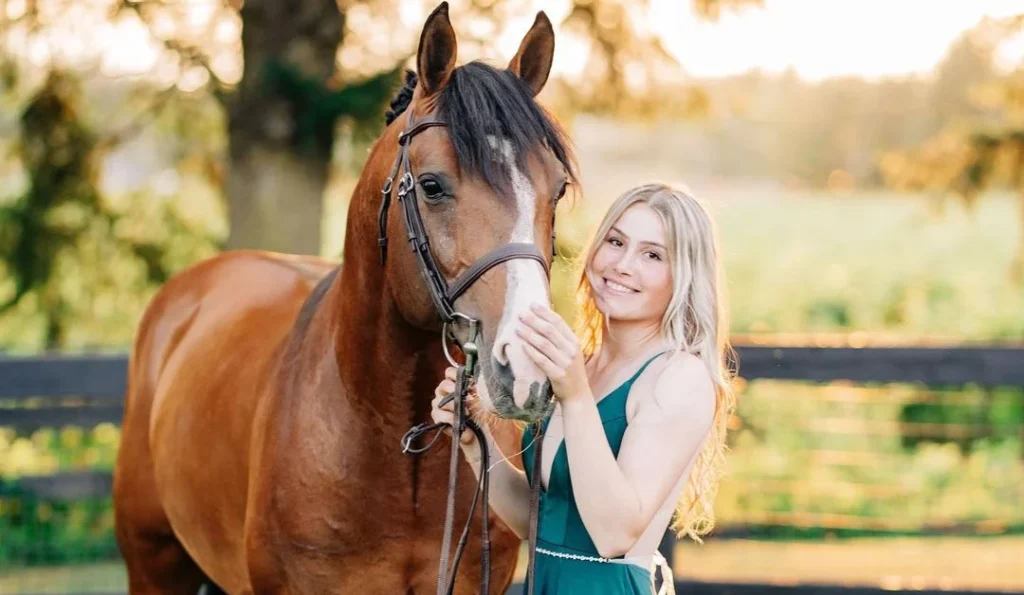 beautiful girl in green dress posing with her horse in a sunny and green landscape for her horse photographer who takes horse photos of her and the brown horse
