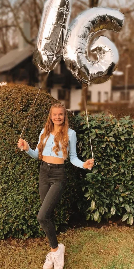 girl posing for her 16th birthday photoshoot. Holding 16th birthday ballons in her garden outside