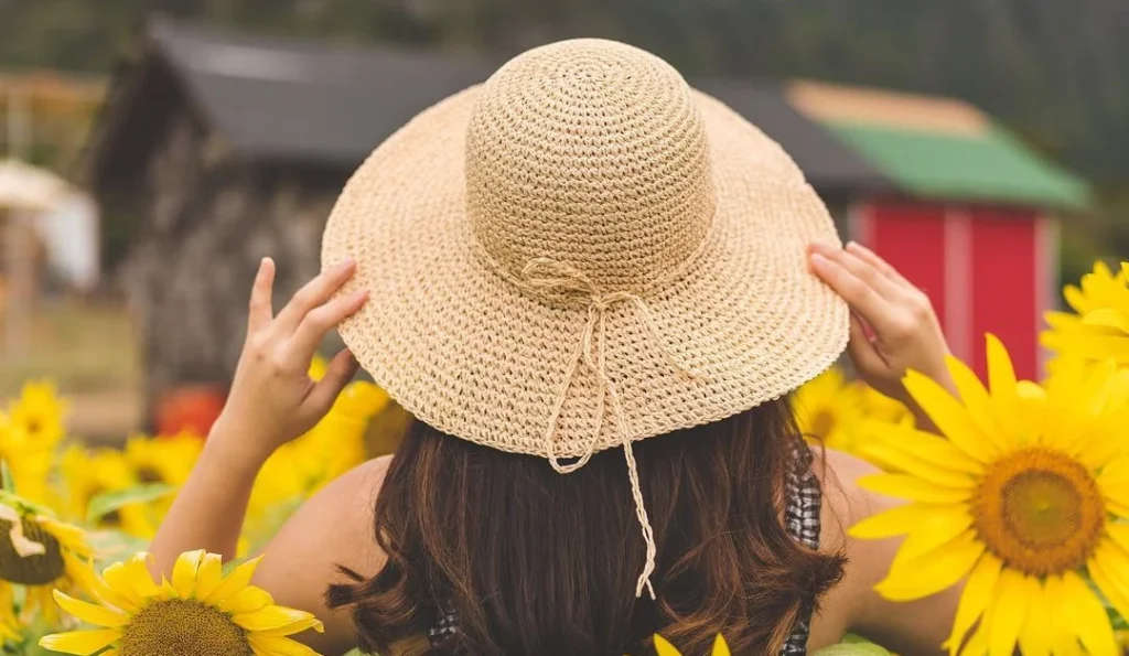 girl holding her straw hat in a field of yellow flowers while doing a portrait of her back