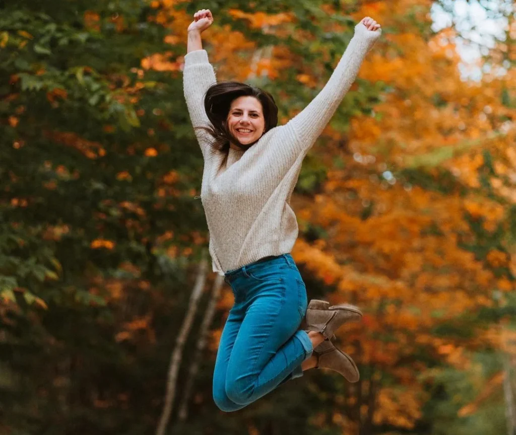 woman jumping into the air in an autumn or fall setting, putting her arms in the air to create a dynamic picture