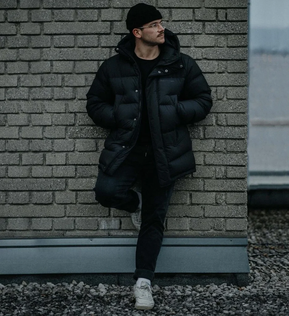 man leaning on a wall, wearing dark outfit, looking away from camera to create a cool photo