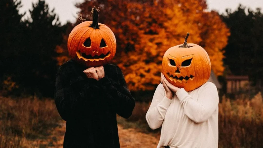 couple wearing carved pumpkins on their heads doing funny poses and creating a cute fall setting
