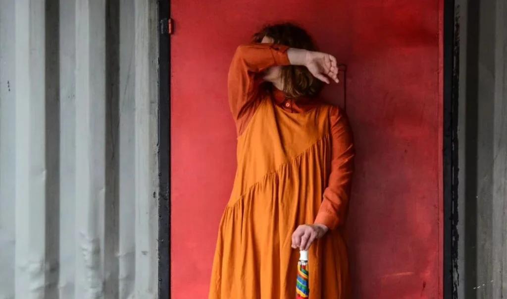 woman in orange holding her arm in front of her face to create a pose for a faceless portrait photography photoshooting