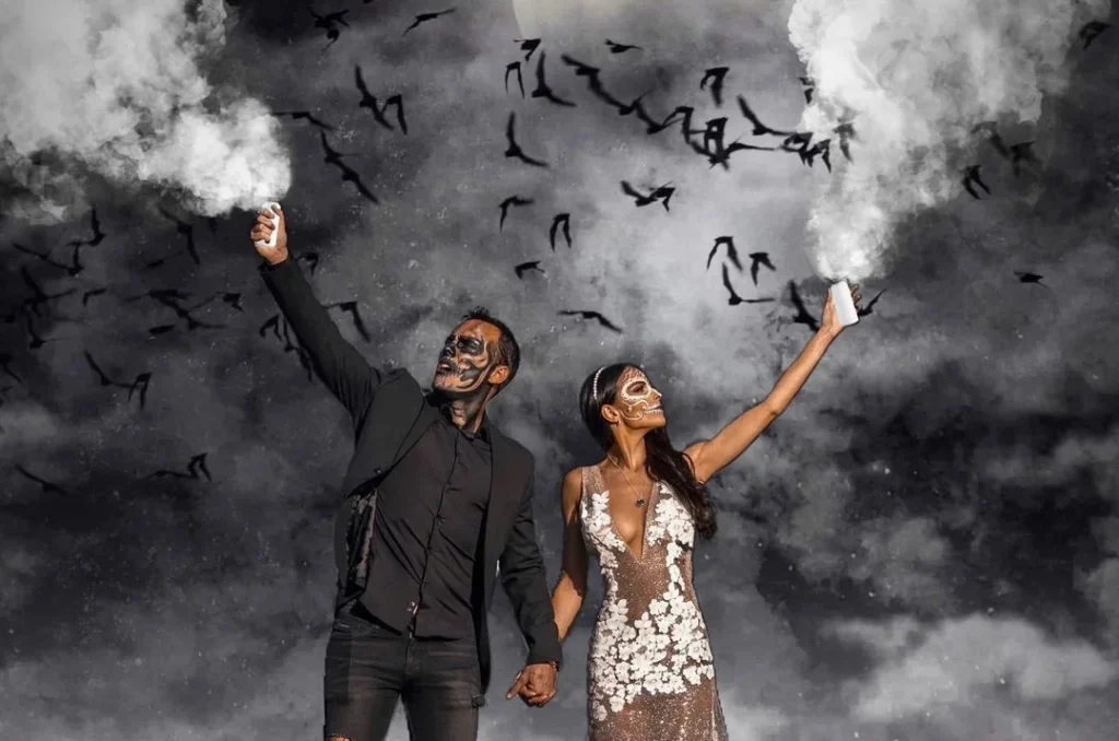 couple blowing scary steam into the air while raven fly by in the full moon, they are wearing scary costumes for their couple halloween photoshooting
