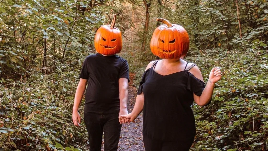 cute couple wearing pumpkins as halloween costumes, walking in a forest to pose for cute couple photos for halloween