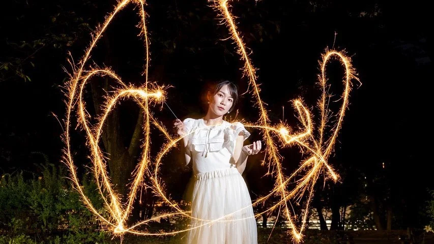cute asian girl posing for photos at night with two long sparklers, creating stunning light effects for the camera