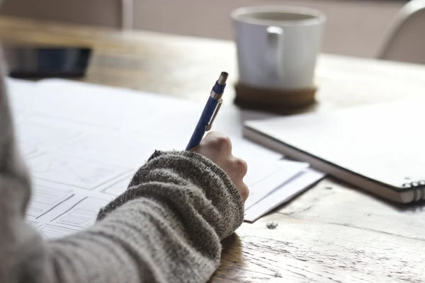 hand writing on a piece of paper, coffee mug in the background