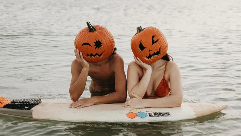 Couple swimming at a lake wearing pumpkin heads to do a cute pumpkin head couple photoshoot wearing pumpkin heads.