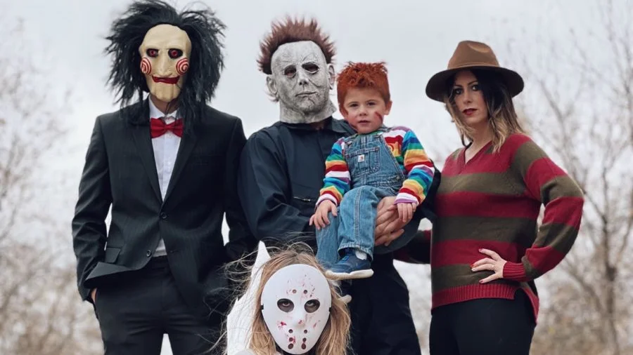 family posing for a family halloween photoshoot outdoors, dressed up as famous halloween figures with masks and toddlers and babys