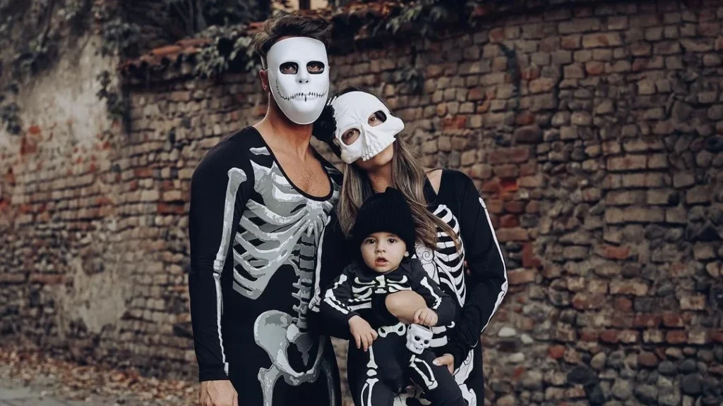 family halloween outfit of skeletons, parents posing with their child for a spooky halloween family photo
