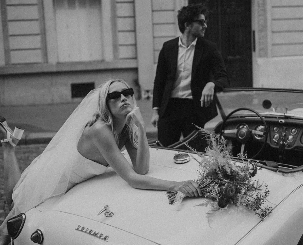 vintage wedding photography of a couple that posing on an oldtimer car with flowers and a vintage wedding dress