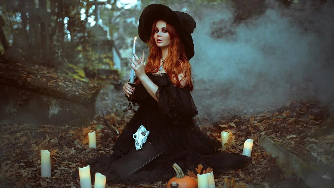 witch sitting outside with candles and a pumpkin, posing for a witchy photoshoot