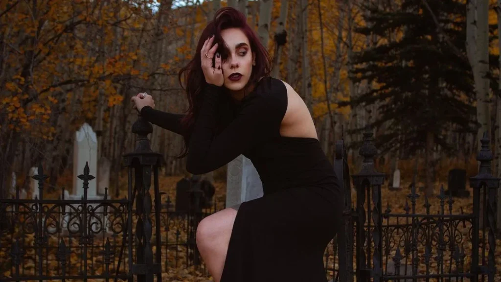 woman at graveyard posing for halloween photoshoot ideas. Black pretty dress with free back, playing with hair, cemetery as location