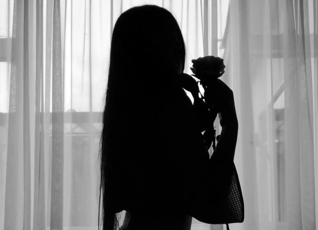 woman holding a rose in front of a curtain, in a dark silhouette from a sensual boudoir shooting