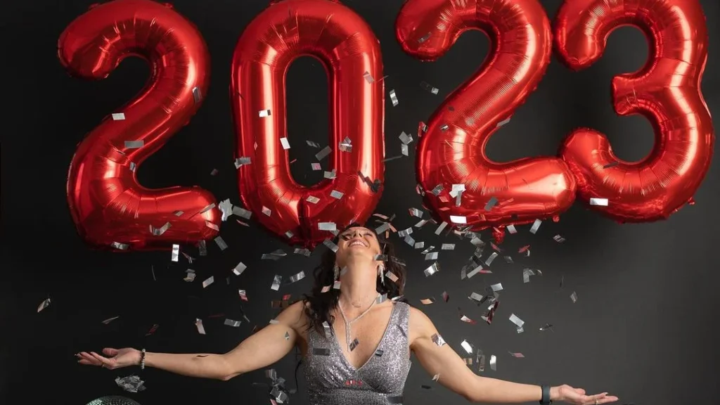 woman posing in front of red new years eve ballons, throwing confetti into the air, laughing and embracing new year photoshoot ideas