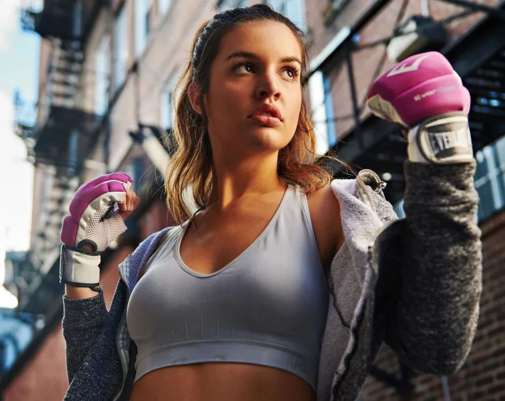 strong boxer girl posing in an urban setting with pink gloves. Bottom angle for a more powerful appearance