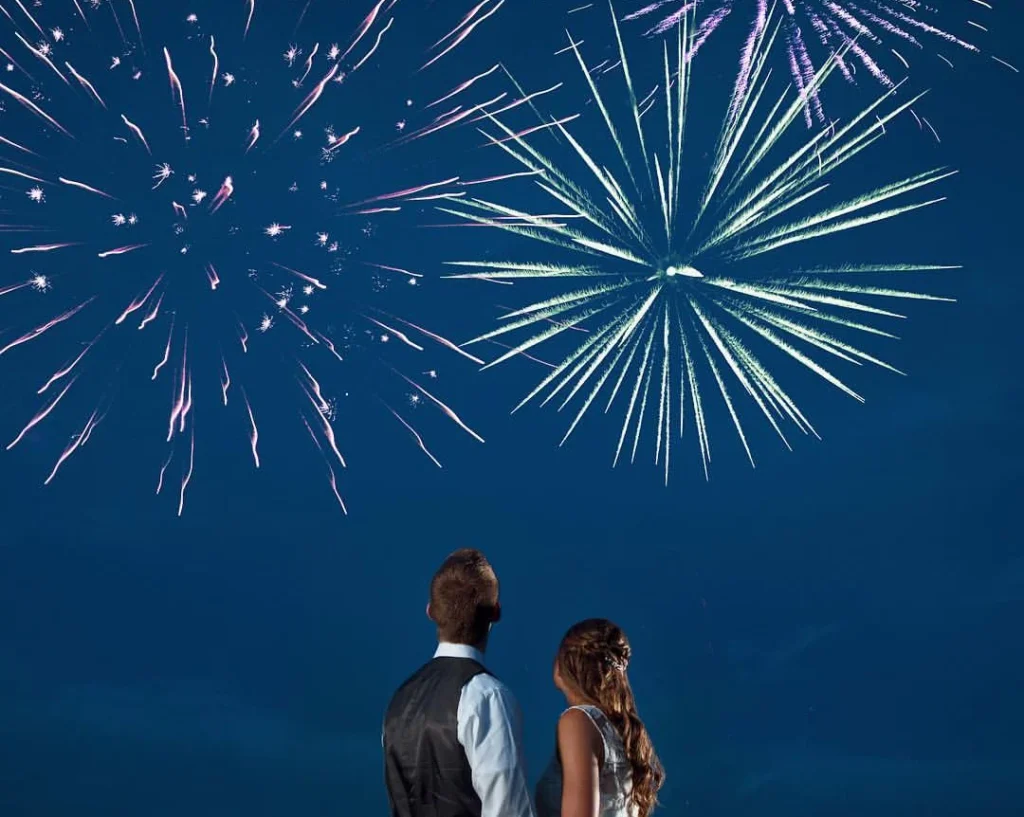 couple watching a romantic firework on new years eve, while holding hands, wearing fancy clothes and posing for the camera
