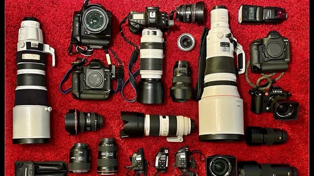 photography equipment with a lot of cameras and lenses lying on a red background