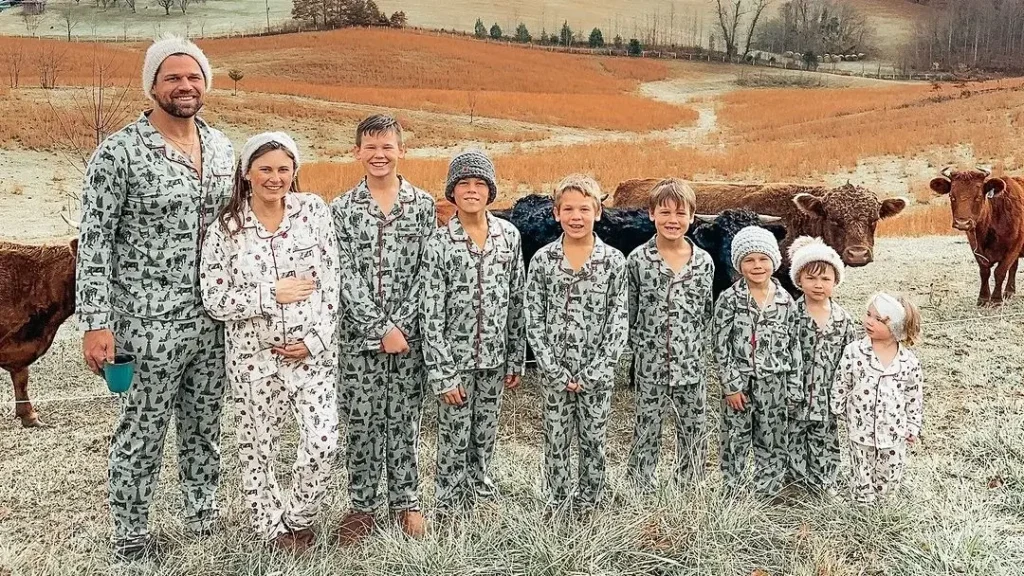 large family photo poses for a big family in green military like pyjamas posing in front of cows doing an outside family photoshoot