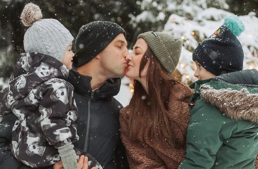 happy family doing winter family photoshoot and posing with their two kids while kissing in the snow