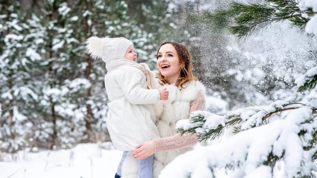 girl posing with her daughter in a winter setting with snow falling of the leaves of a tree