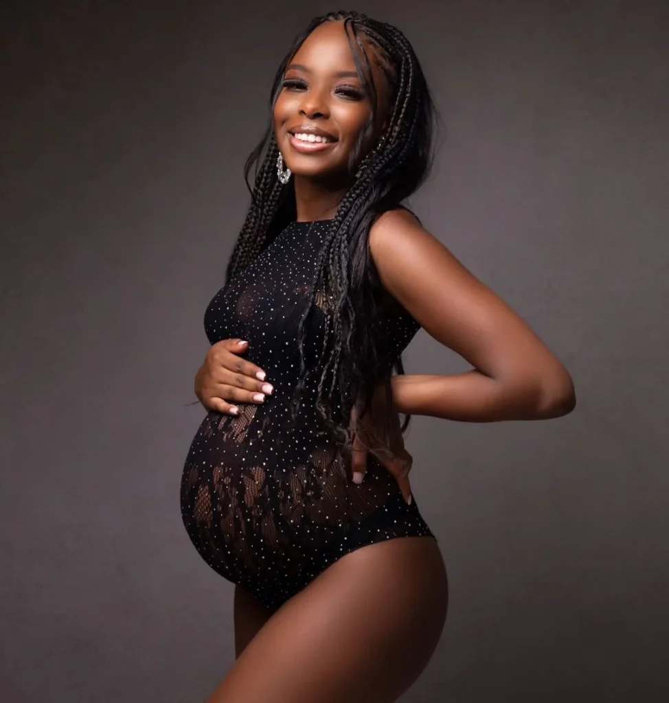 a black woman doing a maternity photoshoot in front of a black background in a black dress, classic pose