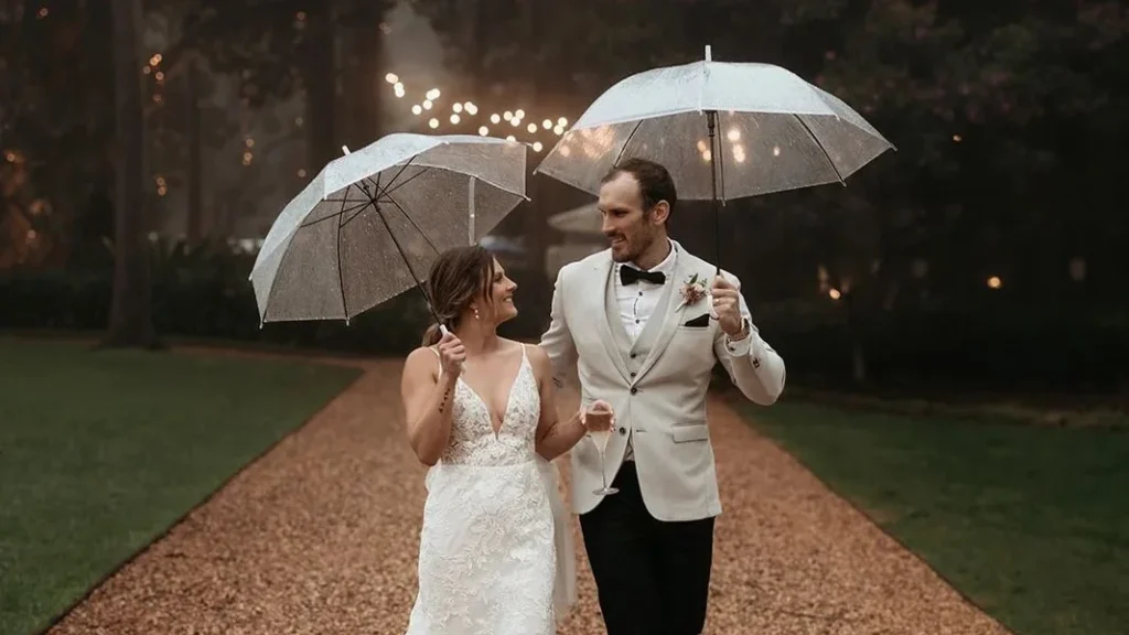 cute married couple walking a path at night while having moody wedding photography and holding an umbrella while looking at each other