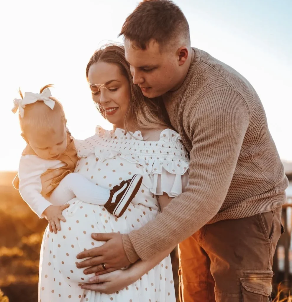 cute young pregnant family with a baby doing a pregnancy photoshoot and pose by holding the belly and cuddle with each other
