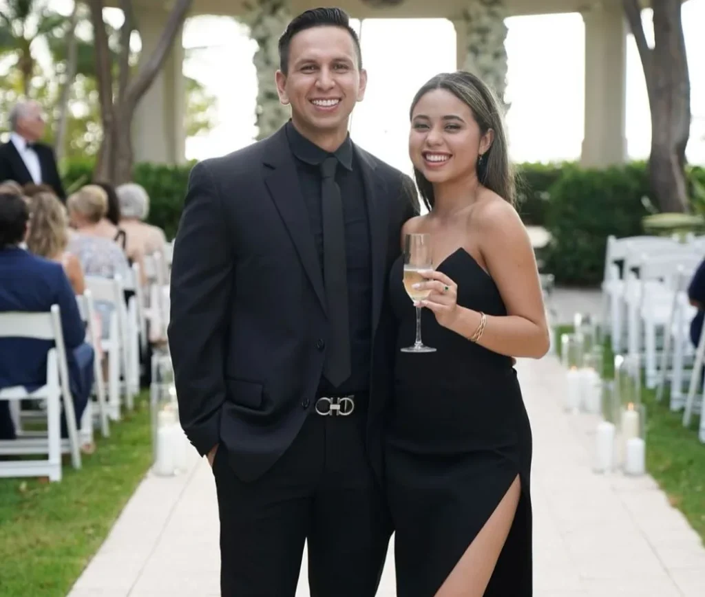 formal dressed couple posing on a wedding for the photographer, holding a glass of champagne and smiling with their black outfits