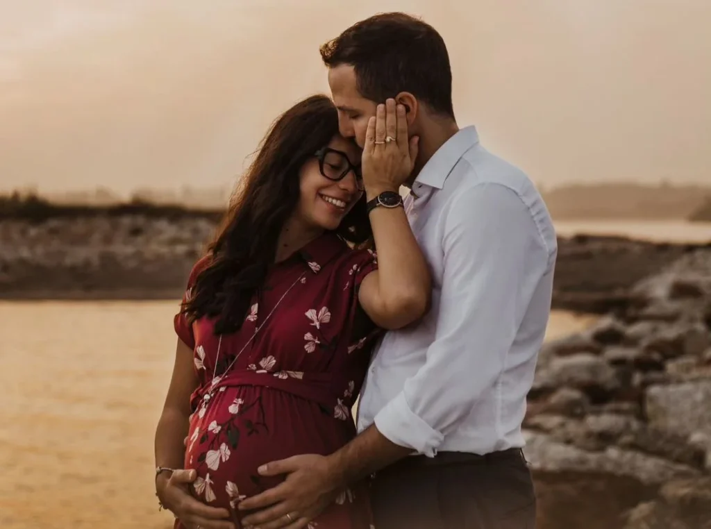 cute young couple having an intimate moment while holding the pregnant belly of the woman and posing for the camera of the photoshoot