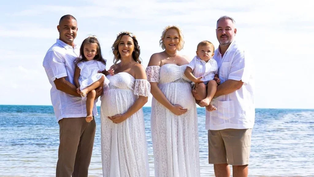 two families with two kids posing for a pregnancy photoshoot, two pregnant witfes in their wedding dresses doing poses with their bump