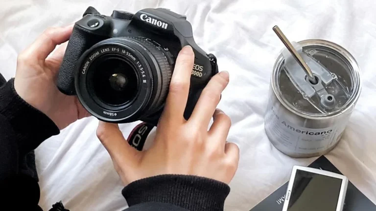 girl holding the best canon camera for beginners on her bed next to a cup of coffee