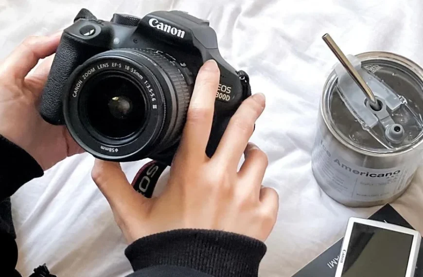 girl holding the best canon camera for beginners on her bed next to a cup of coffee