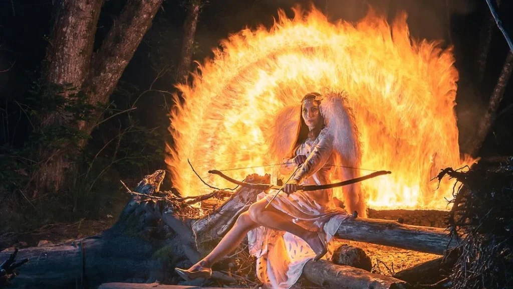 woman dressed as an angel with a bow and wings posing for long exposure photography with fire behind her, used with the exposure