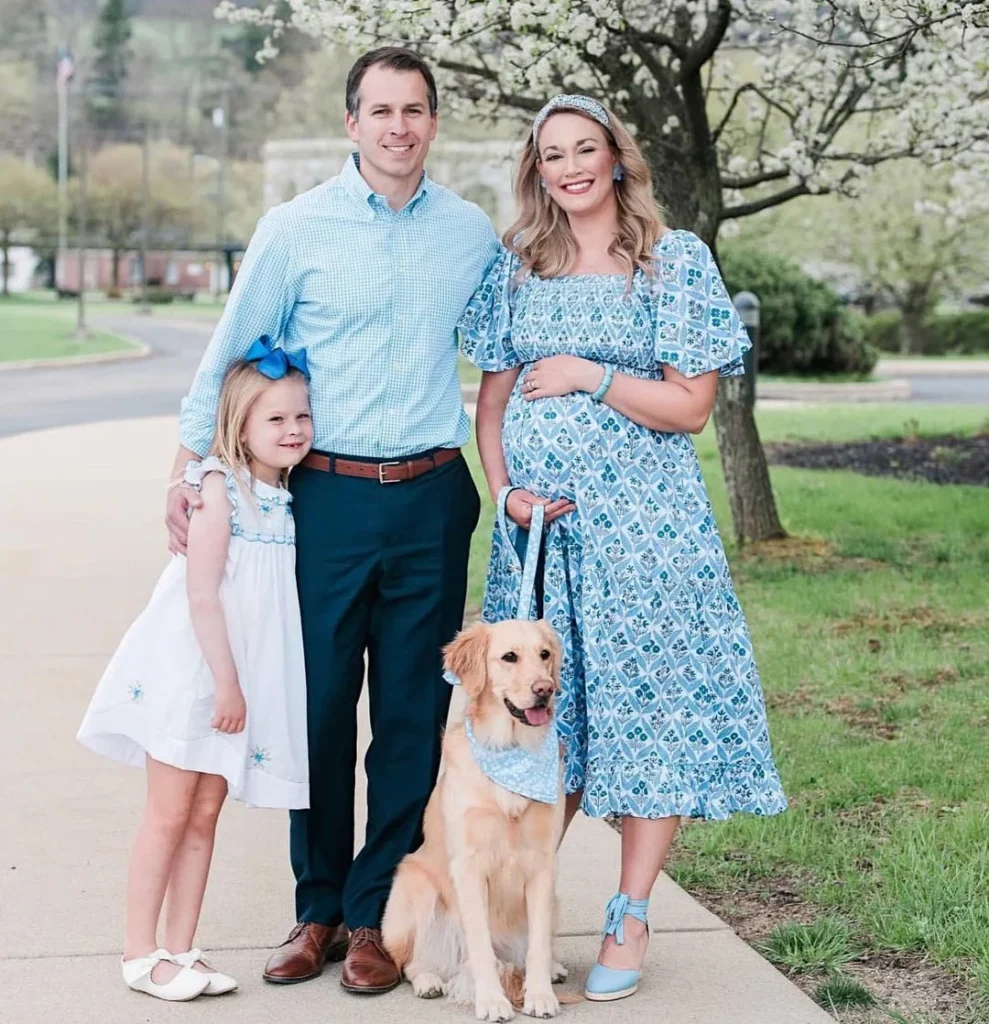 family with dog posing for family spring photoshoot in front of a blossoming flower tree, matching blue sundresses, pregnant photoshoot, happy family