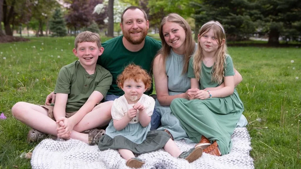 family in green matching spring outfits posing for their family photo in spring on a blossoming meadow, three children, sitting pose on a blanket