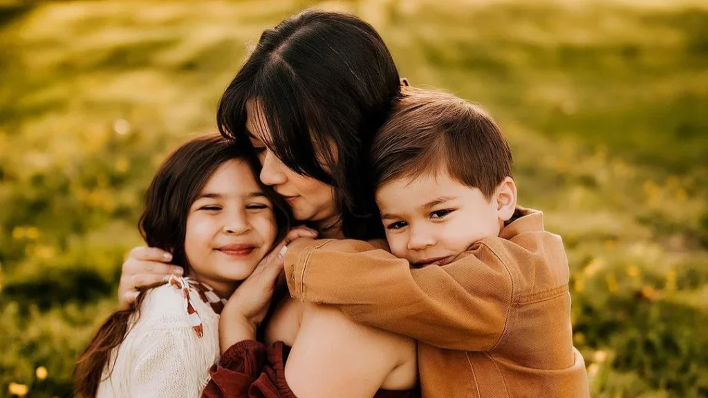 young woman with two children posing on a spring meadow for a family spring photoshoot